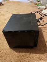 Side view of black Synology DiskStation NAS on carpeted surface showing top panel and attached cables.