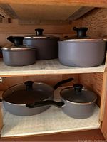 5 T-Fal pots and pans with lids arranged on shelves, showing handles, lids, and interior of cookware.