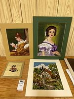 Four textile art pieces displayed on a wooden surface against a wood-paneled background: three larger matted unframed works and one smaller matted piece.
