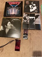 Six vinyl records on carpet including John Lennon & Yoko Ono 'Double Fantasy', Triumph 'Stages' Double Live Album, two unopened U2 albums, and a U2 (RED) Tour collectible badge/lanyard.