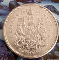 Reverse side of the coin showing the crowned Canadian coat of arms with flags, lions, and maple leaves, dated 1961, with denomination 50 cents.