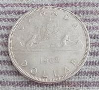 Reverse side of the 1962 Canadian silver dollar showing Voyageur canoe design with two men paddling and year 1962 marked below.