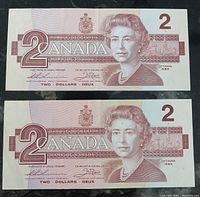 Front side of two 1986 Canadian $2 bank notes featuring Queen Elizabeth II portrait with signatures and denomination.