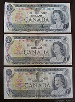Front side of three 1973 Canadian one dollar bank notes stacked showing Queen Elizabeth II and bank details.