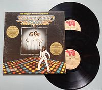 Front cover of Saturday Night Fever 2 album vinyl set with two vinyl records partly visible.