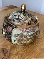 Image showing the round porcelain jar with lid, highlighting the detailed painted cranes and flowers, gold trimmed lid with knob.