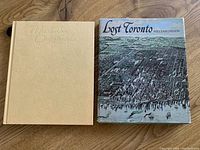 Pair of hardcover coffee table books: Lost Toronto with dust jacket showing aerial illustration of Toronto and beige covered Muskoka Originals book