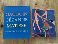Two coffee table art books side by side on wooden surface. Left book has blue cover titled 'Gauguin Cézanne Matisse Visions of Arcadia'. Right book displays colorful art on cover with title 'Impressionism and Post-Impressionism from the USSR'.