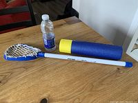 Lacrosse toy and foam super soaker sprayer on wooden table with water bottle for scale