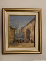 Framed oil painting depicting an Orientalist market scene with a mosque in the background, gold-colored frame and beige matte visible.