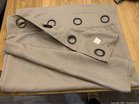 Folded taupe curtain panel on wooden surface showing antique bronze metal grommets at the top edge.