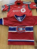 Two toddler sports jerseys laid flat, Montreal Canadiens in front with Toronto FC behind.