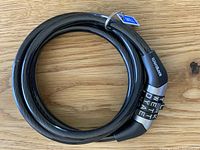 Black coiled cable bike lock with combination dials showing letters on a wooden surface.