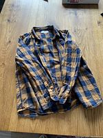 Blue and tan checkered flannel shirt laid flat on wood surface, showing full front and long sleeves.