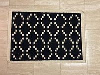 Full view of the rectangular black and white woven rug on tiled floor.