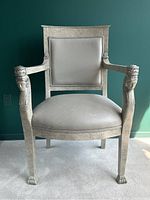 Front view of the vintage wooden armchair showing grey leather seat and back with faux stone finish on wooden structure and carved Egyptian face on arm supports and claw feet.