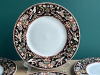 Close-up front view of a Gallo design bone china dinner plate showing intricate colorful floral and bird border on black background with white center