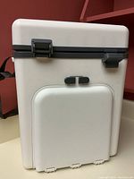 Front view of the white insulated cooler showing two black latches and the closed cutlery compartment.