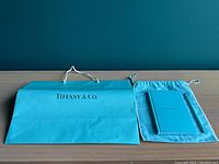 Blue Tiffany & Co. paper shopping bag with white rope handles next to a turquoise cloth bag with notebook and pencil.