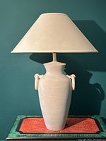 Front view of tall off-white vintage pottery vase lamp with plain conical fabric shade