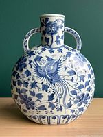 Full view of the vintage blue and white porcelain vase showing round body with handles and painted floral and phoenix bird motif.