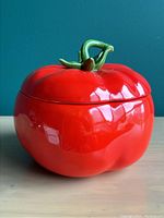 Front side view of bright red ceramic tomato cookie jar with green stem lid.