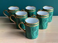 Group of six green malachite-pattern mugs with gold handles and rims