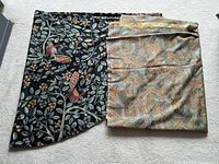 Two fabric pieces laid out: black round tablecloth with bird and floral design on left, multicolor woven tapestry fabric on right folded.