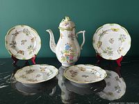 Overview of tea pot and four plates arranged on black surface against teal background