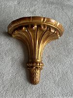 Full view of the carved wall shelf showing fan-shaped top and rounded edges in gilt finish.
