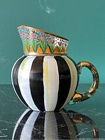 Side view of pitcher showing hand painted floral design and striped body with gold handle and rim