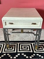 Front view showing pickled oak top, single drawer with brass handles, and steel base with brass feet.
