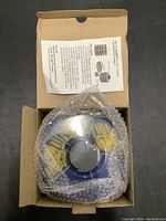 Open cardboard box showing round blue fix-it caddy wrapped in bubble wrap with instruction sheet inside the lid.