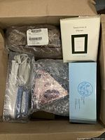 Top view of lot showing clog slippers wrapped in plastic, Sheffield Home picture frame box, Avon beauty products in bubble wrap, and blue boxed candle set.