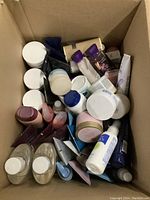 Overhead photo of open cardboard box filled with many bottles, jars, and tubes of body lotions and creams from multiple brands including Bath and Body Works.