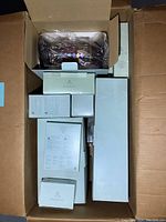 Top-down image of an open box filled with various boxed candles and candle accessories including candle coasters, a large column candle holder, and different types of candles.