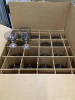 Open cardboard box containing 18 clear wine glasses separated by cardboard dividers.
