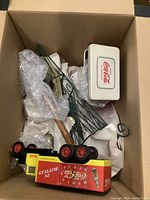 Photo showing the lot inside an open box: Coca Cola tin clock, metal hanging decor, toy truck, grill accessory with wooden handle, and Coca Cola box.
