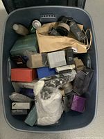 Top-down view of plastic bin filled with various boxed and loose cosmetics and skin care products in different packaging styles and colors.
