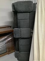 Side view of a dark gray upholstered three-seat couch with a folded-down middle console showing built-in cup holders, placed against a wall near wooden furniture.