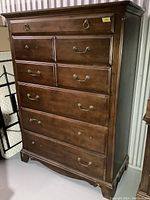 Full view of brown wooden chest of drawers showing seven drawers and missing handles on some.