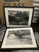 Photo of two framed black and white landscape photographs, one propped upright and the other laying in front, showing the full image and framing details
