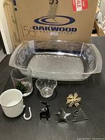 Clear holly platter with Christmas-themed mugs, small cups, and metal napkin rings in festive shapes placed inside the platter for display