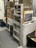 Silver aluminium ladder standing upright, multiple steps visible, placed next to other household items.