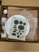 Top view of cardboard box containing wrapped Mikasa china pieces and illustration sheet showing silhouette outlines of the various china items included in the set.
