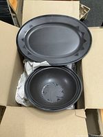 Top down view of grey Pfaltzgraff oval platter and matching bowl inside a cardboard box with wrapping paper.