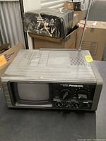 Front angled view of vintage Panasonic portable TV with knobs, small screen, extendable antenna, and ventilation slots on top. Showing some dirt and usage signs.