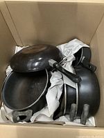 Photo showing four pots and pans stacked together inside a box with paper cushioning.