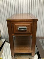 Photo showing the wooden side table with a drawer and lower shelf, highlighting the metal handle and top surface.