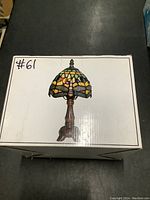 Photo of boxed Tiffany style stained glass lamp showing product image on box with a colorful stained glass shade and bronze base.